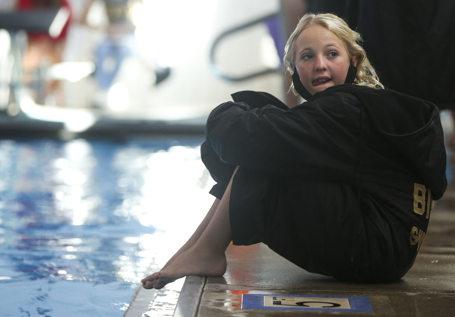 Hannah Southerland sits on the edge of the pool watching the early races
